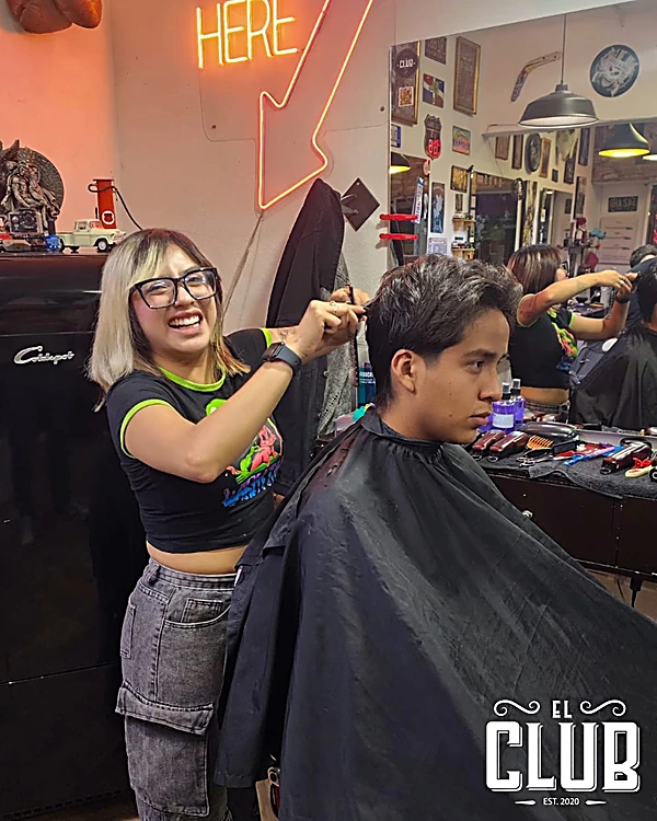 Barbera sonriendo mientras peina y corta el cabello de un cliente