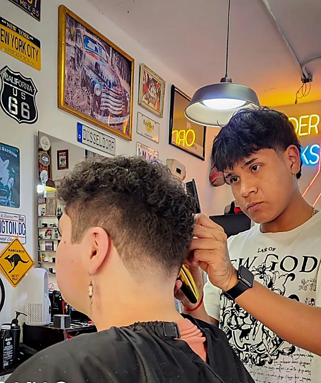 Barbero cortando frente a la pared de placas de New York City, Route 66 y Washington DC