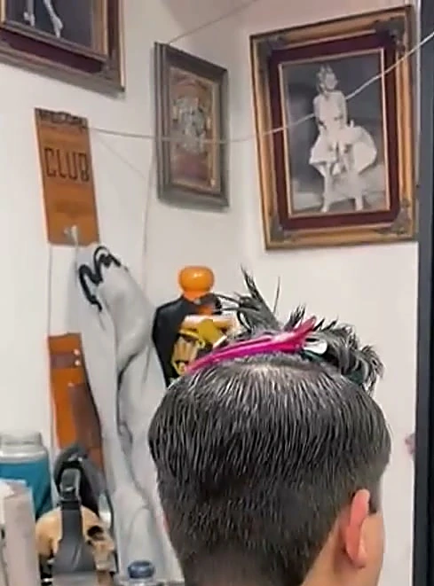 Cuadro de Marilyn con marco dorado y una placa de El Club en la pared, sobre un cliente con pinzas en el cabello