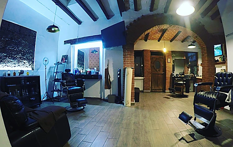 Interior de El Club: vigas de madera, arcos de ladrillo, piso de madera y sillones de barbero de piel negra